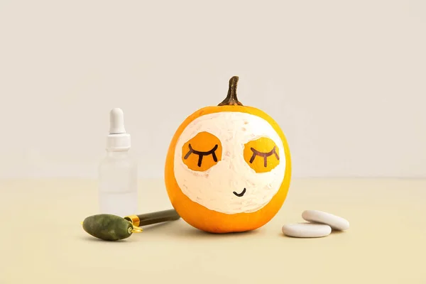 Pumpkin with mask, facial massage tool, cosmetic bottle and spa stones on beige background