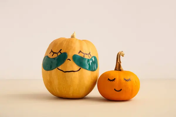 Pumpkins with drawn faces and under-eye patches on beige background