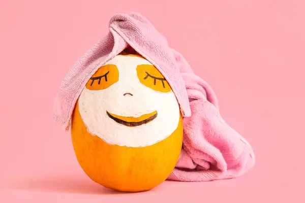 Pumpkin with drawn face, mask and towel on pink background
