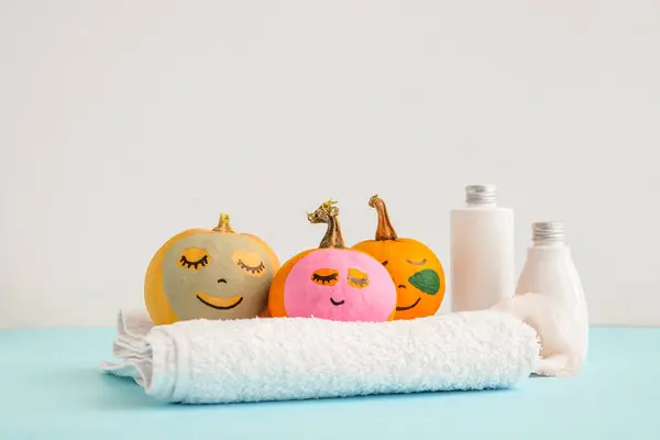 Pumpkins with under-eye patches, masks, towel and cosmetic bottles on blue table