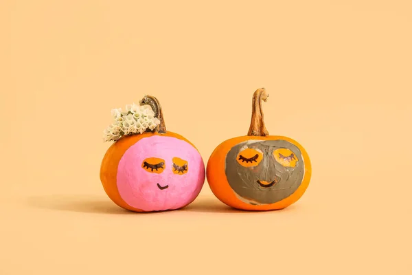 Pumpkins with masks and flowers on beige background