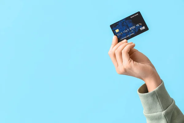 Young woman with credit card on blue background, closeup
