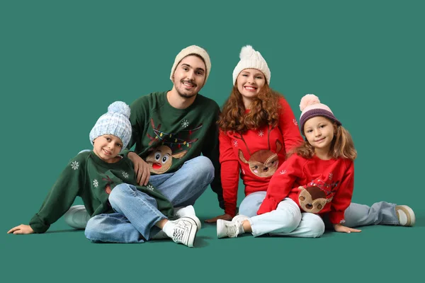 Happy family in warm sweaters sitting on green background