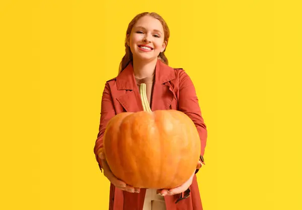 Young woman with pumpkin on yellow background