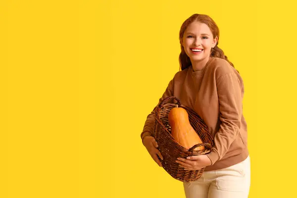 Young woman with pumpkin in basket on yellow background