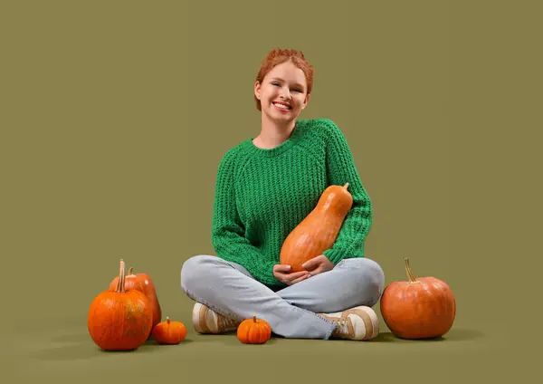 Young woman with pumpkins sitting on green background