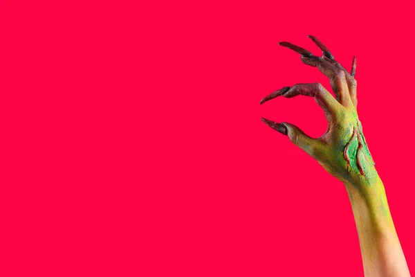 Hand of witch with claws on red background. Halloween celebration