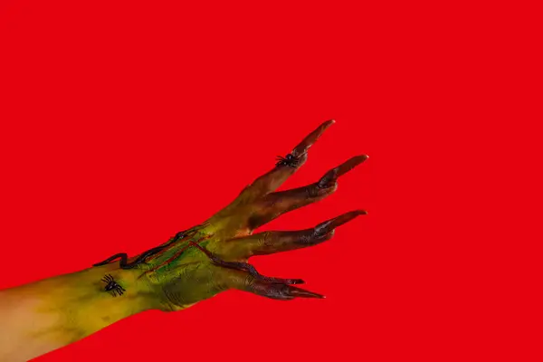 Hand of witch with claws on red background. Halloween celebration