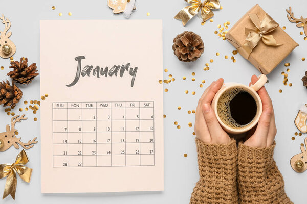 Paper calendar for January with Christmas decorations and woman drinking cup of coffee on grey background