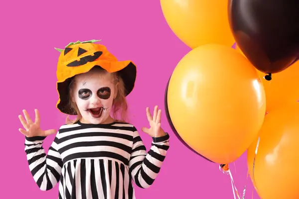 Little girl dressed for Halloween with balloons on purple background