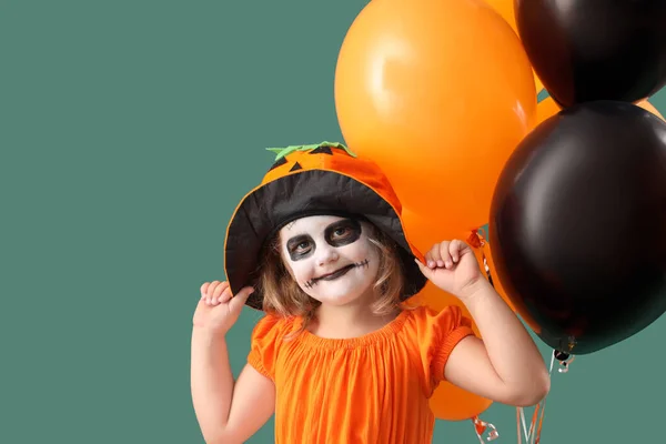 Little girl dressed for Halloween with balloons on green background