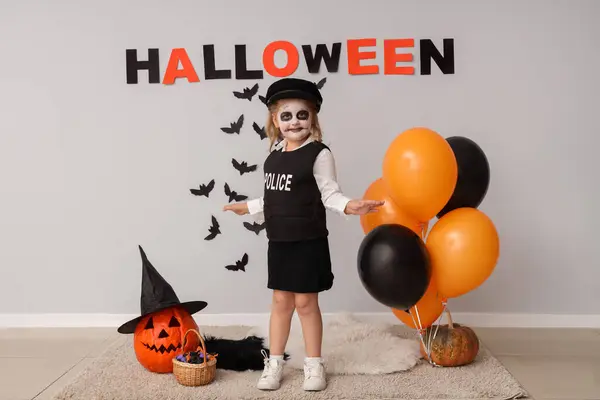Little girl dressed for Halloween with balloons and decor near light wall