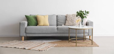 Rahat gri kanepe, yastıklar ve vazoda çiçekli süs, ışık duvarının yanındaki masada.