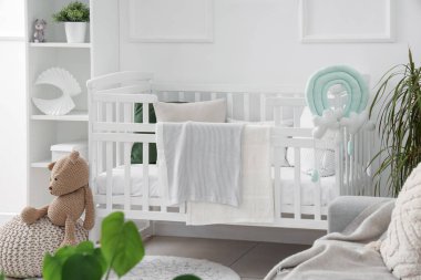 Bebek yatağı ve raf ünitesi olan beyaz tonlu çocuk odasının şık bir iç mekanı.