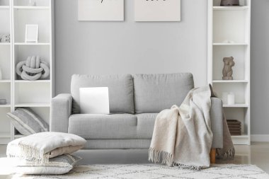 Aydınlık oturma odasının içinde modern dizüstü bilgisayarı olan rahat gri kanepe.