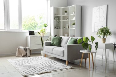 Işıl ışıl oturma odasının içi rahat gri kanepe ve çiçeklerle dolu.