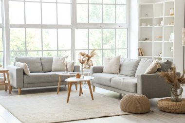 Işıl ışıl oturma odasının içi. Büyük pencerenin yanında rahat gri koltuklar ve kahve masası.