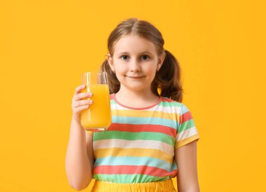 Sarı arka planda bir bardak portakal suyu olan tatlı küçük kız.
