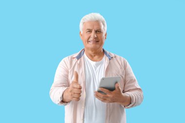 Tablet bilgisayarı olan son sınıf öğrencisi mavi arka planda baş parmağını kaldırıyor.