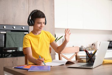 Kulaklık ve dizüstü bilgisayarı olan küçük çocuk mutfakta internetten ders çalışıyor.