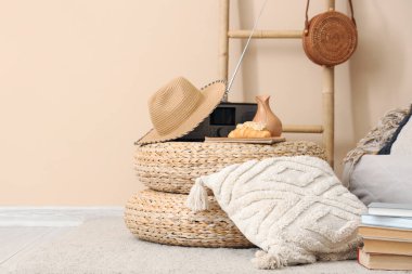 Hasır puf, yastık, şapka ve radyo bej duvarın yanında.