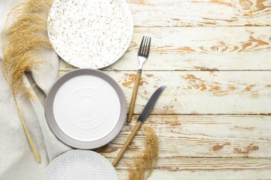 Temiz tabaklar, çatal bıçak takımı ve beyaz ahşap masada kurutulmuş çimenler.