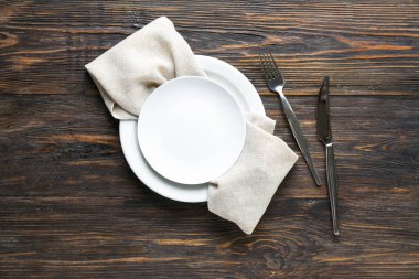 Temiz tabaklar, çatal bıçak takımı ve peçete ahşap masada.