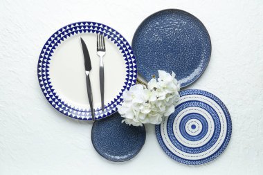 Temiz tabaklar, çatal bıçak takımı ve çiçekler beyaz masada.