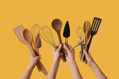 Sarı arka planda farklı pişirme aletleri olan kadın elleri.