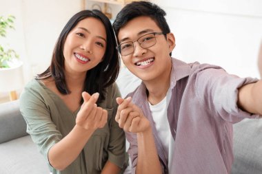 Genç Asyalı arkadaşlar evde kalp hareketi yapıyorlar, yakın plan.