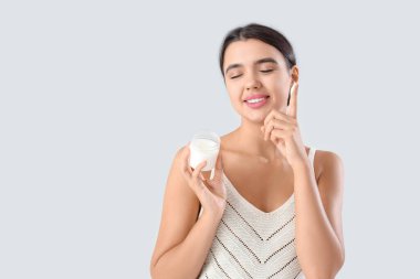 Gri arkaplana karşı vücuduna hindistan cevizi yağı süren güzel bir kadın.