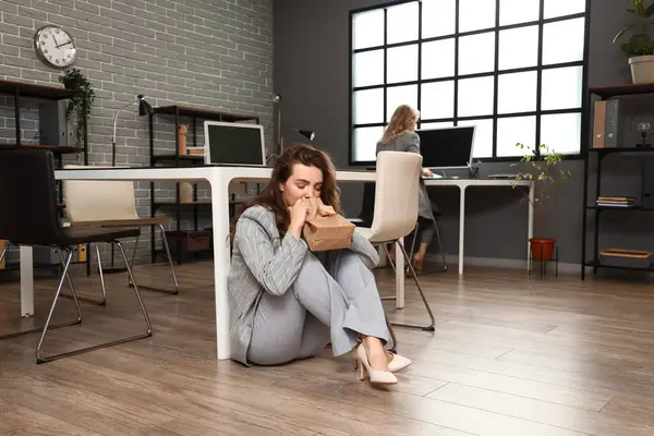Young woman with paper bag having panic attack in office