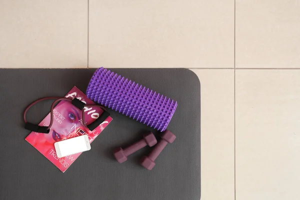 Sports equipment with mobile phone and magazine on fitness mat in gym, top view