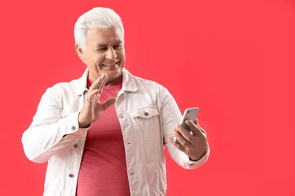 Senior man with mobile phone video chatting on red background