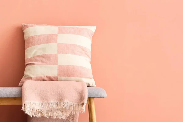 Grey bench with cushions and blanket near pink wall
