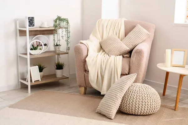 Hafif oturma odasının içinde yastıklı ve battaniyeli rahat bir koltuk.