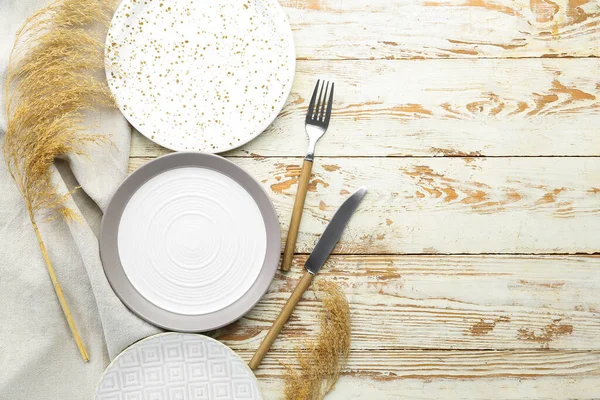 Clean plates, cutlery and dried grass on white wooden table