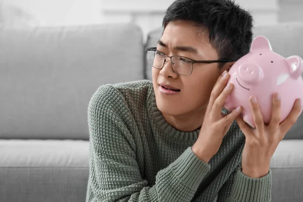 Young Asian man with piggy bank at home, closeup