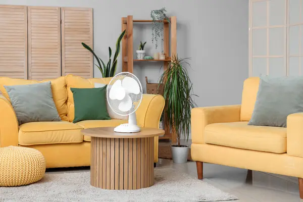 Interior of living room with yellow sofas and electric fan on wooden coffee table