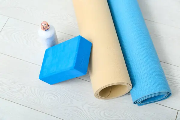 Yoga mats, foam exercise block and bottle of water on floor in gym, closeup