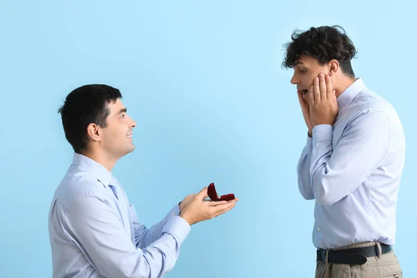 Young man proposing to his boyfriend on blue background