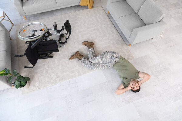 Young soldier with PTSD lying on floor at home, top view