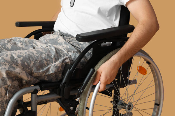 Young soldier in wheelchair on beige background, closeup