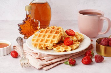 Böğürtlenli waffle, akçaağaç şurubu ve beyaz arka planda bir fincan çay.