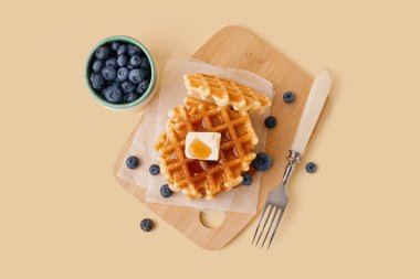 Sarı zemin üzerinde yaban mersini ve akçaağaç şurubuyla lezzetli waffle tahtaları.