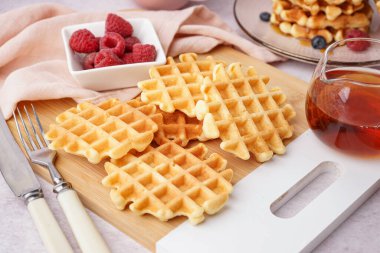 Ahşap ahududu ve beyaz arka planda akçaağaç şurubuyla lezzetli waffle tahtaları.