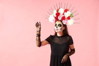 Pembe arka planda boyalı kafatası olan genç bir kadın. Meksika Ölüler Günü (El Dia de Muertos) kutlamaları