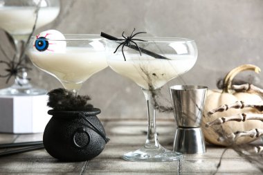 Gri arka planda Cadılar Bayramı kutlamaları için lezzetli beyaz kokteyller ve ölçü bardakları yakın plan.
