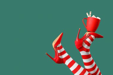 Yeşil arka planda bir fincan kakaolu Noel çoraplı genç kadın.