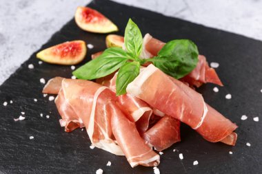 Gri arka planda lezzetli prosciutto dilimleri olan tahta